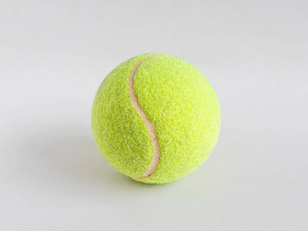 Leuchtend gelber Tennisball aus Filz und Gummi, zum Rasentennis, liegt auf hellem Hintergrund - Foto, Bild