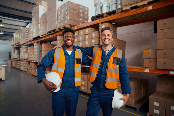 Smiling portrait of two multi ethnic warehouse workers holding safety hardhat in hand at factory - Foto, immagini