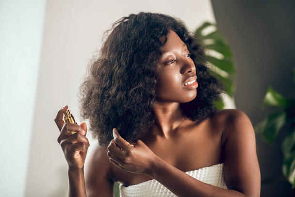 Appealing african american woman spraying serum on her hair - Fotografie, Obrázek