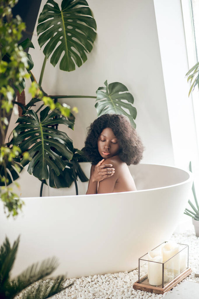 Dark-skinned woman relaxing in a bath and washing her body - Foto, afbeelding