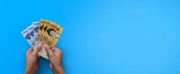 Two hands holding korean won banknote on blue background. Finance business and banking concept. - Фото, изображение