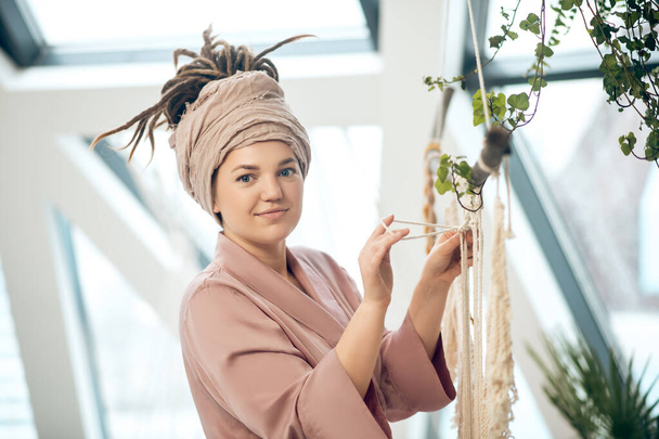 Young woman in a headwear weaving macrame and looking positive - Foto, imagen