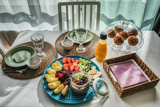 Close-up van mediterrane maaltijd of ontbijt met biologische muffins en seizoensfruit op witte houten tafel en elegante omgeving met rustieke stromatten. De continentale snack is versierd met Chia pudding en sinaasappelsap op houten witte achtergrond - Foto, afbeelding