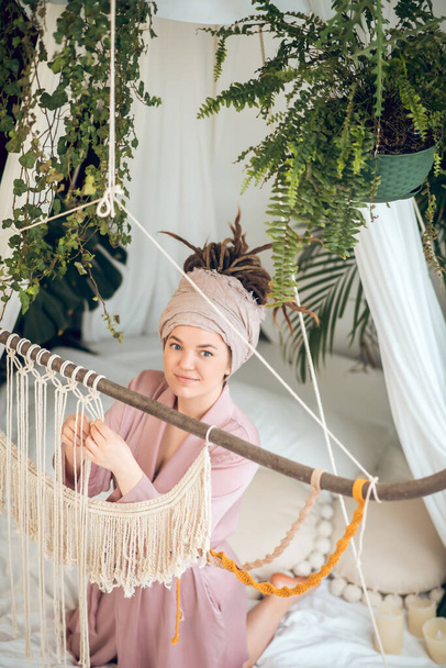 Young woman in a headwear looking busy while weaving macrame - 写真・画像