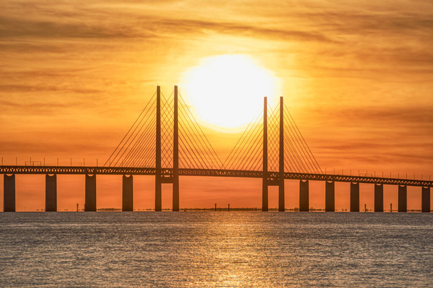 バルト海のオレンジ色の橋暖かい夕日、中央のパイロンの詳細とケーブルで構造。スウェーデンのコペンハーゲン、デンマーク、マルモの間のリンクや接続は、北欧諸国や北欧諸国の間のギャップを埋めるために構築されました - 写真・画像