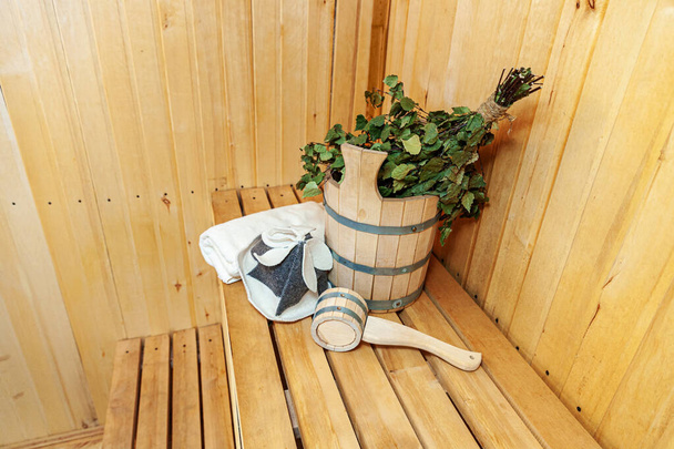 Interior details Finnish sauna steam room with traditional sauna accessories basin birch broom scoop felt hat towel. Traditional old Russian bathhouse SPA Concept. Relax country village bath concept. - Photo, Image