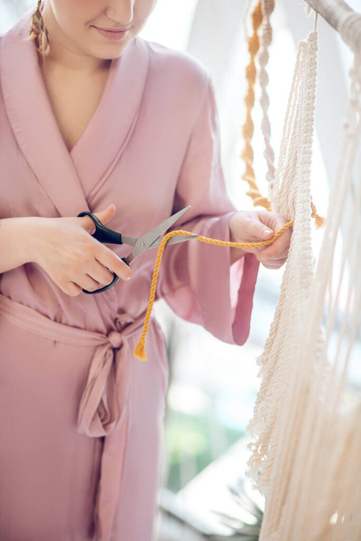 Woman in a headwear cutting yarn while weaving macrame - Φωτογραφία, εικόνα