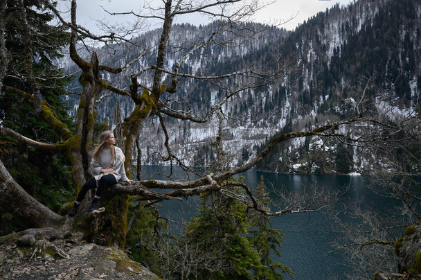 Girl sits on a tree and meditates near lake Ritsa in Abkhazia - Foto, afbeelding