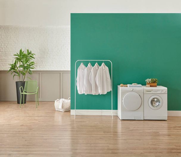 Wasmachine en droger ruimte, wit schoon shirt, groene muur en decoratieve achtergrond, linnen mand. - Foto, afbeelding
