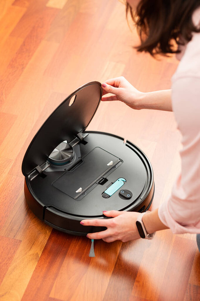 Faceless middle section of young woman opening an automatic vacuum cleaner to clean the floor, machine housework robot - Photo, Image