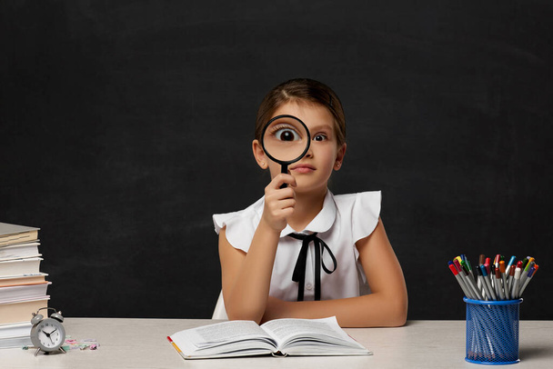 cute little schoolgirl looking through magnifying glass - Photo, Image