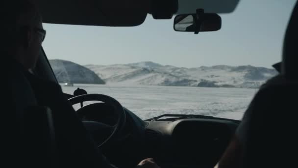 Mies ajaa autoa talvitiellä lumipeitteisten vuorten takana. Näkymä tuulilasin läpi - Materiaali, video