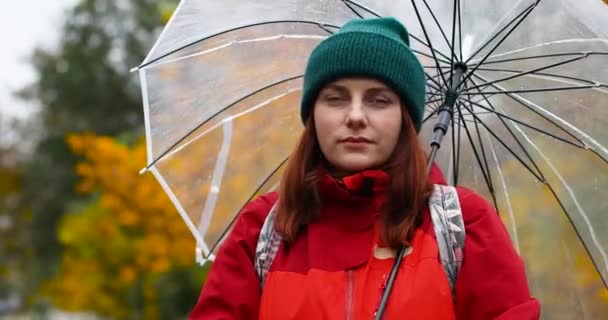 Kırmızı ceketli ve şeffaf bir şemsiye altında yağmurlu havanın tadını çıkaran bir kadın. Sonbahar havası, sarı yapraklar - Video, Çekim