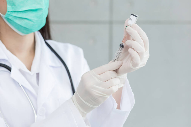 Kobieta lekarz używa strzykawki do wysysania szczepionki (szczepionki Coronavirus) z butelki, podczas gdy jej ręce noszą gumowe rękawiczki i maskę do twarzy.. - Zdjęcie, obraz