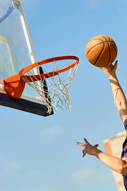 Close-up of a guy throwing a basketball into the basket against the blue sky. - Foto, Bild