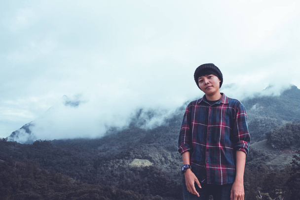 Ázsiai fiatalember skót ingben és fekete kalap túrázás hegycsúcs felett felhők és köd túrázó szabadban. Doi Luang Chiang Dao Chiangmai tartomány, reggel. - Fotó, kép