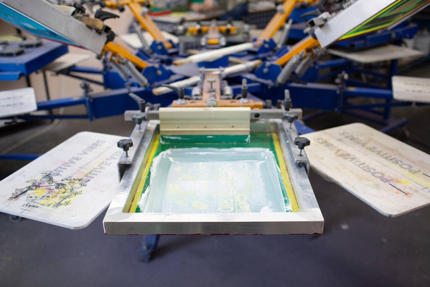 Serigrafia processo de impressão de tela de seda na fábrica de roupas. Moldura de carrossel, espremedor e tintas coloridas de plastisol - Foto, Imagem
