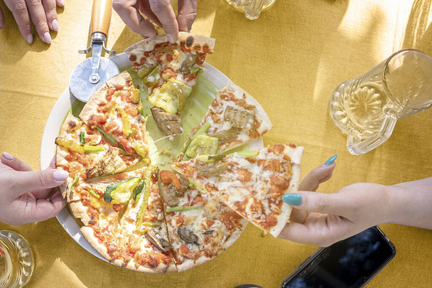 友達と共有するテーブルの上でピザを切る。イタリア料理で祝う自由時間 - 写真・画像
