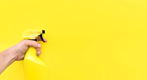 Primer plano de la mano de la persona con pulverizador de limpieza aislado sobre fondo amarillo. Espacio para texto. - Foto, imagen