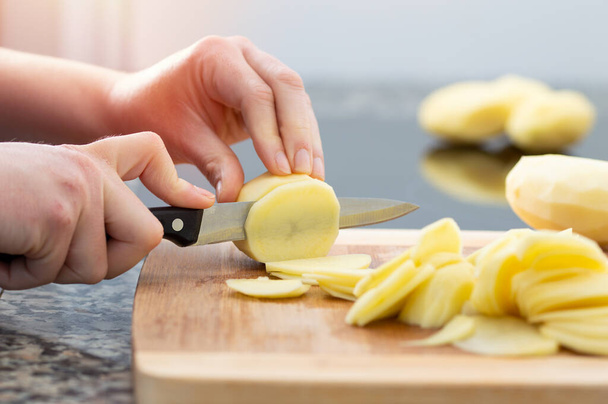 Recortado de cerca plano de una mujer cortando patatas en una tabla de corte.Concepto de preparar una tortilla tradicional española - Foto, imagen