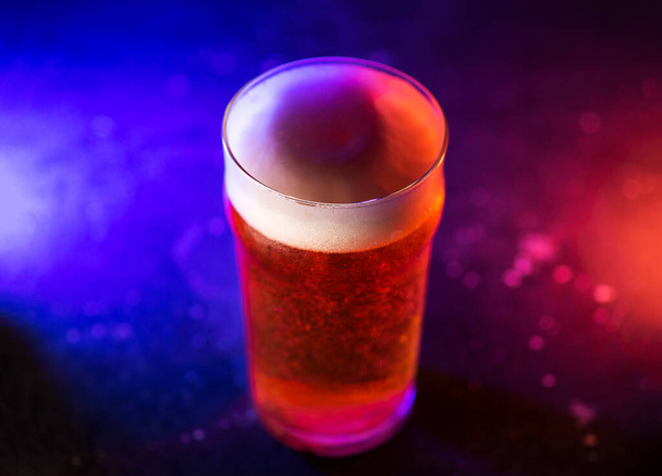 Un verre de bière artisanale sur fond sombre, lumière tendance colorée - Photo, image