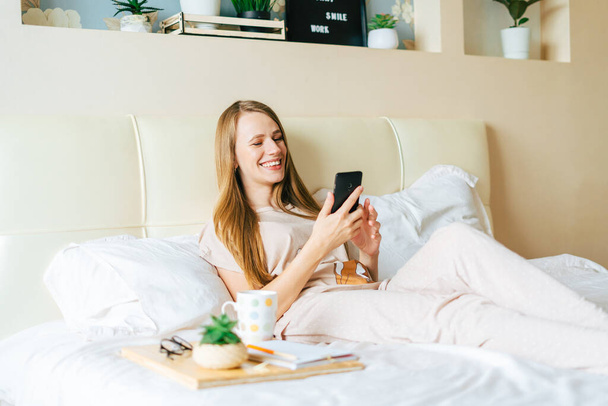 jonge vrouw het nemen van een selfie op smartphone terwijl zitten op bed - Foto, afbeelding