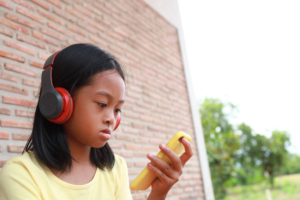 Милая азиатка использует красный беспроводной наушник, чтобы слушать музыку на телефоне. - Фото, изображение