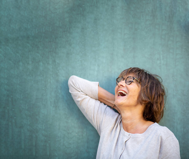 Primer plano retrato mujer mayor riendo con anteojos contra pared verde - Foto, imagen