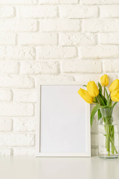 Bukiet żółtych tulipanów w szklanym wazonie i pustej ramce na białej ceglanej ścianie tła. Projekt makiety - Zdjęcie, obraz