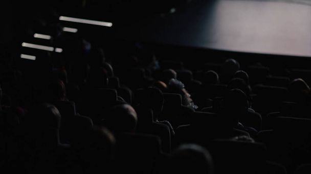 Mensen zitten in de donkere hal en kijken een film. Een video. Achteraanzicht van mensen in de bioscoop kijken naar een film aandachtig, concept van vrije tijd. - Foto, afbeelding