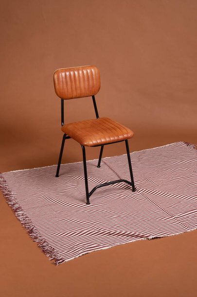 Черный металл и коричневое кожаное кресло на ковре из красных и белых линий на коричневом фоне. - Фото, изображение