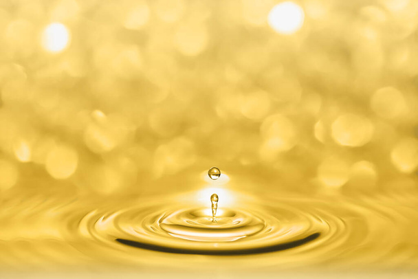 Fotografía macro de gotitas salpicadas de líquido dorado brillando y creando ondas circulares sobre un fondo bokeh brillante. - Foto, imagen
