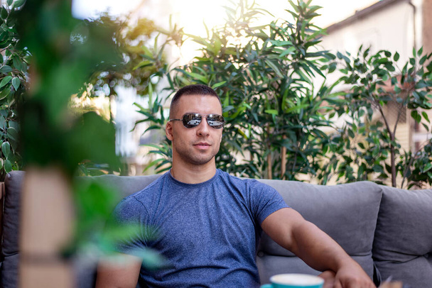 Porträt eines gut aussehenden erfolgreichen smarten Mannes, der Kaffee im Café trinkt. Mann frühstückt sitzend auf schöner Terrasse mit Pflanzen. - Foto, Bild