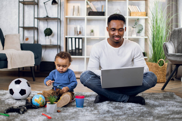 Baby boy playing with toys while father working on laptop - Photo, Image