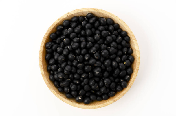 tepelně neupravené černé fazole v dřevěné míse na bílém pozadí - Fotografie, Obrázek