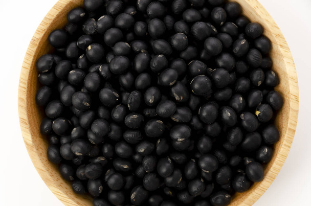 tepelně neupravené černé fazole v dřevěné míse na bílém pozadí - Fotografie, Obrázek