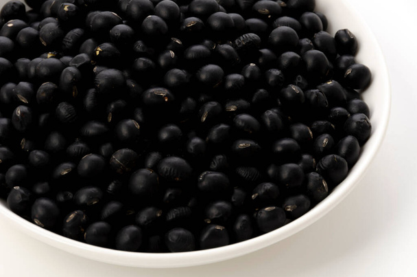 nevařené černé fazole na talíři na bílém pozadí - Fotografie, Obrázek