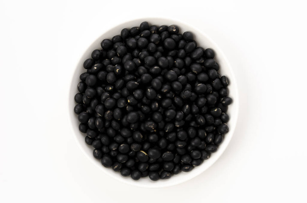 haricots noirs non cuits sur une assiette sur fond blanc - Photo, image