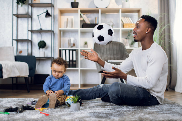 Happy father and son sitting on carpet and playing with ball - Foto, Imagen