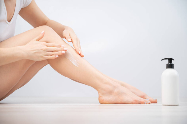 Woman applies moisturizer to her legs on a white background. The girl takes care of the skin and uses the cream. - Foto, imagen