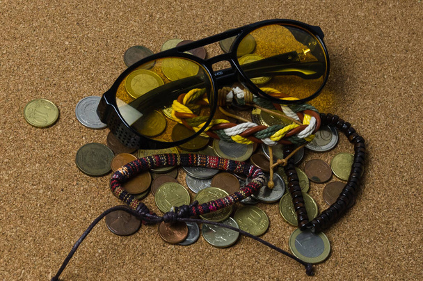 zonnebril met diverse armbanden en munten rusten terloops op de lichtbruine huid - Foto, afbeelding