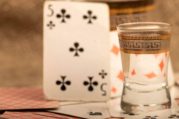Jugando a las cartas y un vaso de vodka en una mesa cubierta con arpillera gruesa. Primer plano, enfoque selectivo. - Foto, imagen