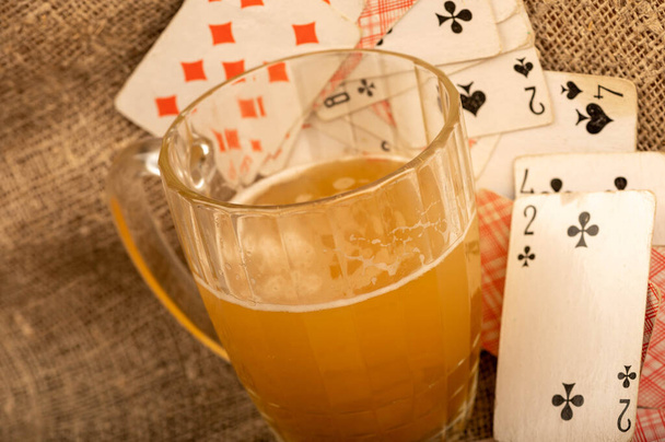 Speelkaarten en een mok licht ongefilterd bier op een tafel bedekt met grove doek. Close-up, selectieve focus. - Foto, afbeelding