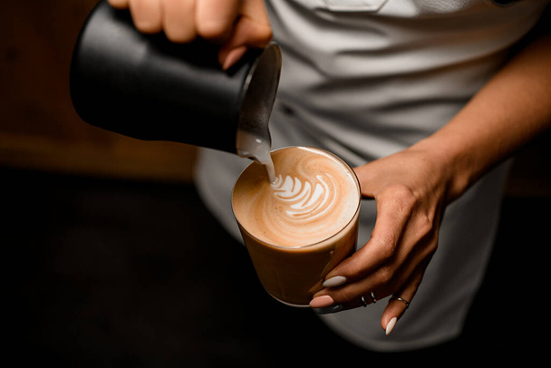 woman barista gently drawing pattern pouring milk into glass with latte drink - Fotoğraf, Görsel