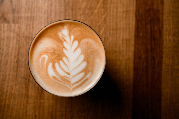 Top view of beautiful white pattern on frothy latte in glass on wooden table - 写真・画像