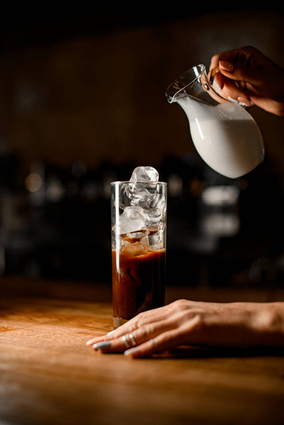 view of glass with cold coffee and ice cubes and womans hand holding it - Фото, зображення