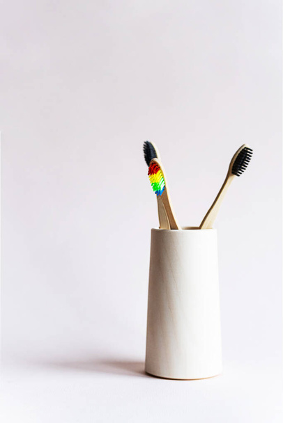 Bamboo toothbrushes in a wooden glass on a light pink background. Minimalistic still life of eco-friendly bathroom products. Zero waste, no plastic, sustainable lifestyle concept. - Photo, Image
