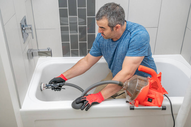 Egy férfi egy mini vízvezeték-szerelő kígyót használ a fürdőkád lefolyójának kibogozására. - Fotó, kép