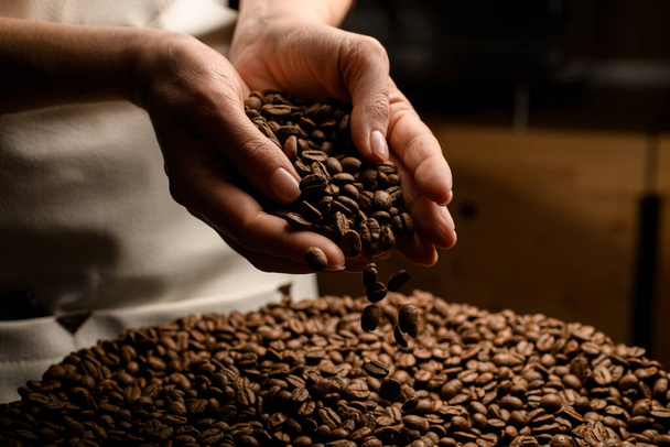 Close-up of womans hands with roasted coffee beans pouring out of cupped hands - Fotó, kép