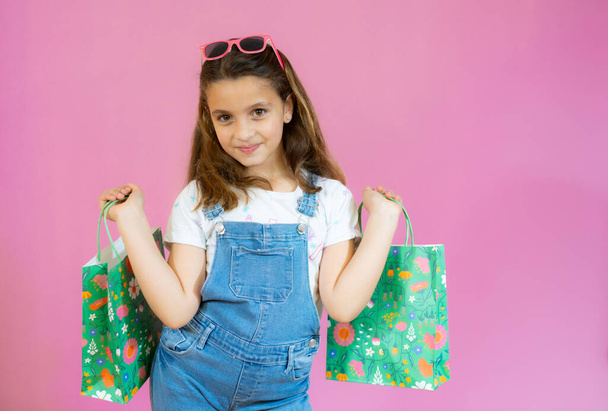 Menina hispânica bonito segurando sacos de compras isolados sobre fundo rosa - Foto, Imagem